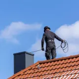 Kominiarz w cylindrze wykonuje przegląd kominiarski na dachu.
