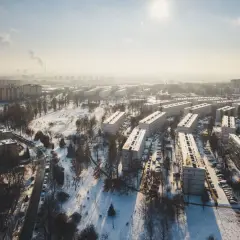 Zimowy krajobraz Krakowa z blokami mieszkalnymi i parkiem. Widać dymiące kominy w oddali, co może wpływać na ceny mieszkań w Krakowie.