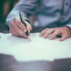 Dłoń pisze długopisem na dokumencie. To ważny wpis do księgi wieczystej, który wymaga precyzji i skupienia.