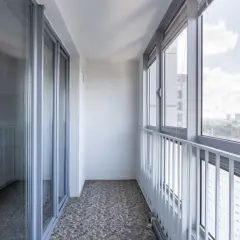 Zabudowa balkonu w bloku z przeszklonymi drzwiami i oknami, oferująca widok na miasto.