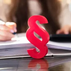 Czerwony znak paragrafu symbolizuje prawo i porządek, podczas gdy w tle osoba pracuje nad dokumentami, co może sugerować kwestie związane z zasiedzeniem.