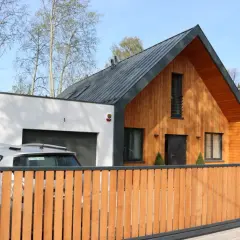 Nowoczesna dobudówka do starego domu, z drewnianą elewacją i garażem. Projekty takich domów łączą tradycję z nowoczesnością.