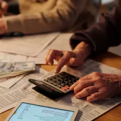Dłonie starszej osoby liczą pieniądze i wpisują dane na kalkulatorze, przygotowując się do zapłaty podatku od spadków i darowizn.