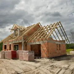 Budowa domu w toku, widoczne ściany z pustaków, drewniany dach i materiały budowlane. Zastanawiasz się, ile kosztuje budowa domu?