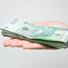 Dłoń trzyma stos banknotów 100 zł. Może to być prezent, ale pamiętaj o podatku od darowizny.