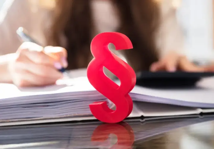 Czerwony znak paragrafu symbolizuje prawo i porządek, podczas gdy w tle osoba pracuje nad dokumentami, co może sugerować kwestie związane z zasiedzeniem.