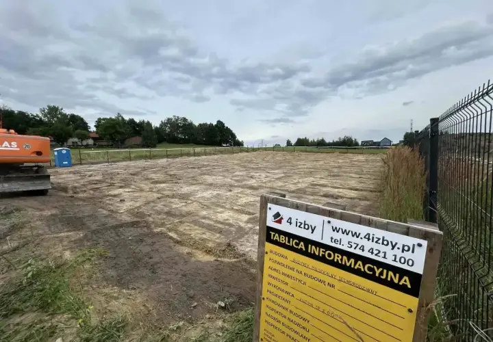 Tablica informacyjna budowy na placu budowy z koparką i toaletą.