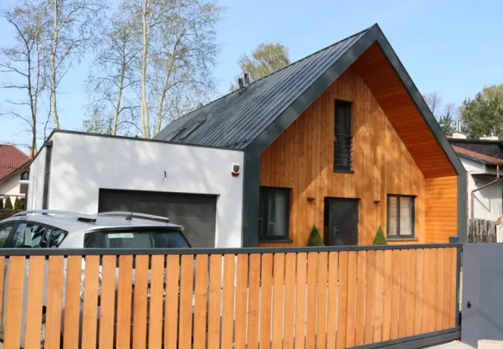 Nowoczesna dobudówka do starego domu, z drewnianą elewacją i garażem. Projekty takich domów łączą tradycję z nowoczesnością.