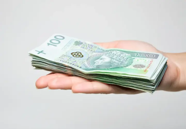 Dłoń trzyma stos banknotów 100 zł. Może to być prezent, ale pamiętaj o podatku od darowizny.