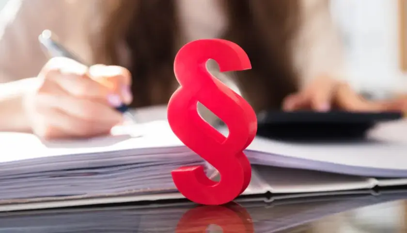 Czerwony znak paragrafu symbolizuje prawo i porządek, podczas gdy w tle osoba pracuje nad dokumentami, co może sugerować kwestie związane z zasiedzeniem.