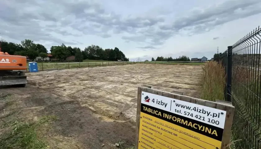 Tablica informacyjna budowy na placu budowy z koparką i toaletą.
