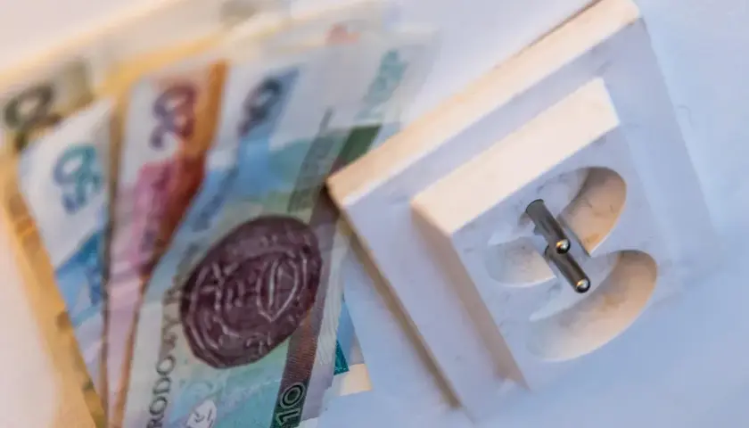 Pieniądze leżą obok gniazdka elektrycznego, symbolizując wysoki rachunek za prąd.