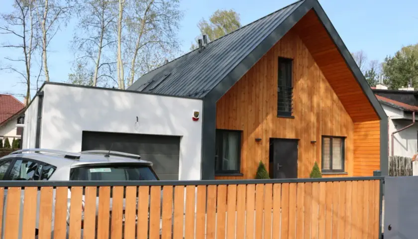 Nowoczesna dobudówka do starego domu, z drewnianą elewacją i garażem. Projekty takich domów łączą tradycję z nowoczesnością.