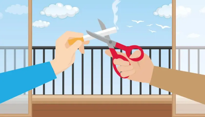 Dwie ręce przecinają nożyczkami papierosa na balkonie. Czy można palić na balkonie? Ta ilustracja sugeruje, że nie.
