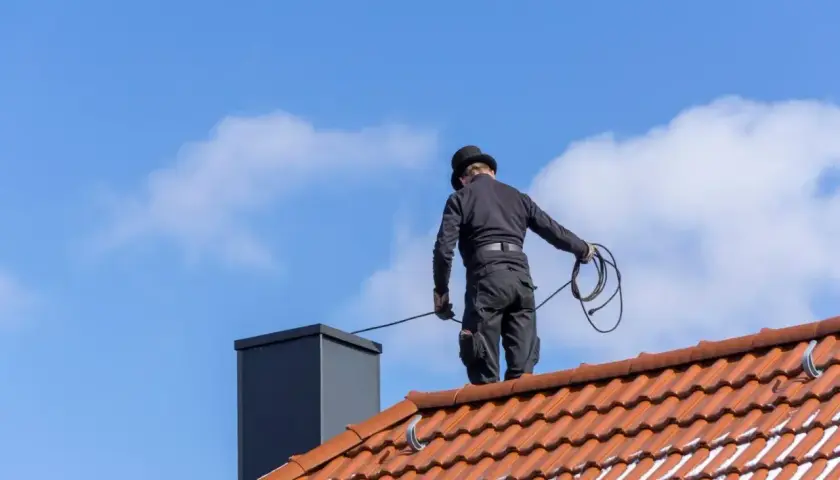 Kominiarz w cylindrze wykonuje przegląd kominiarski na dachu.