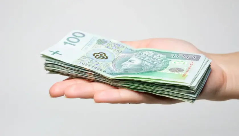 Dłoń trzyma stos banknotów 100 zł. Może to być prezent, ale pamiętaj o podatku od darowizny.