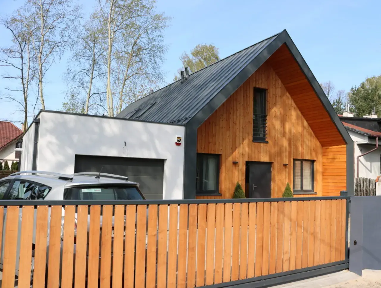 Nowoczesna dobudówka do starego domu, z drewnianą elewacją i garażem. Projekty takich domów łączą tradycję z nowoczesnością.