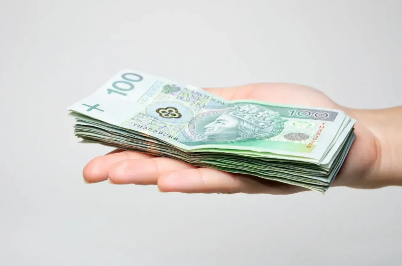 Dłoń trzyma stos banknotów 100 zł. Może to być prezent, ale pamiętaj o podatku od darowizny.